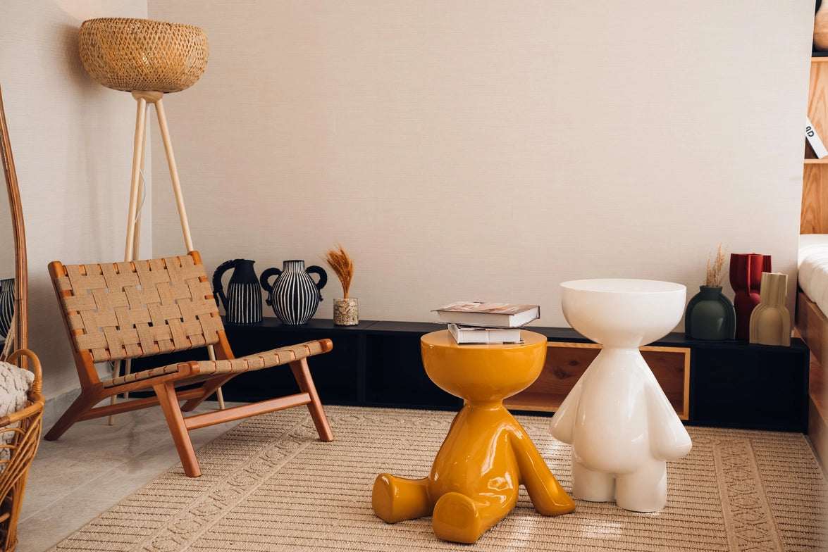 Modern interior with a wooden chair, yellow stool, and white sculpture on a textured floor.